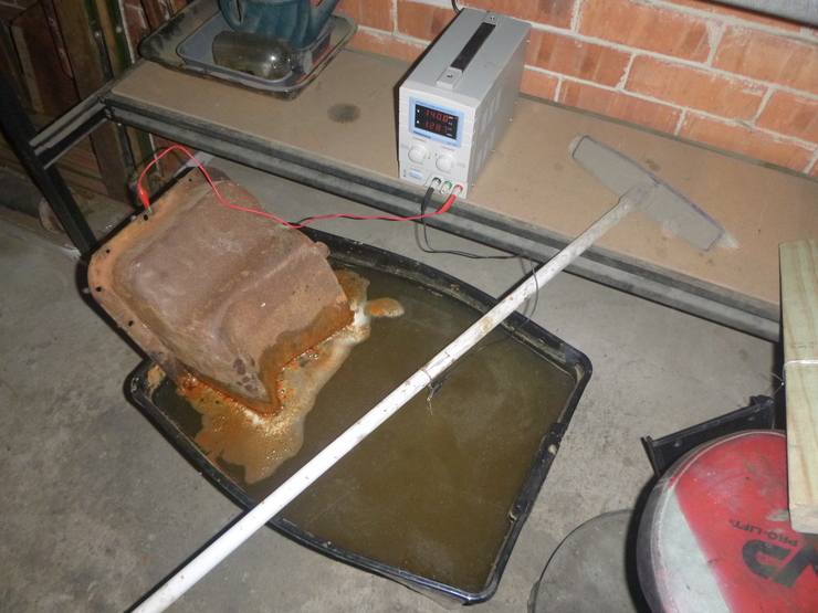 Tub of water with rust scum floating on surface, connected to a DC power supply